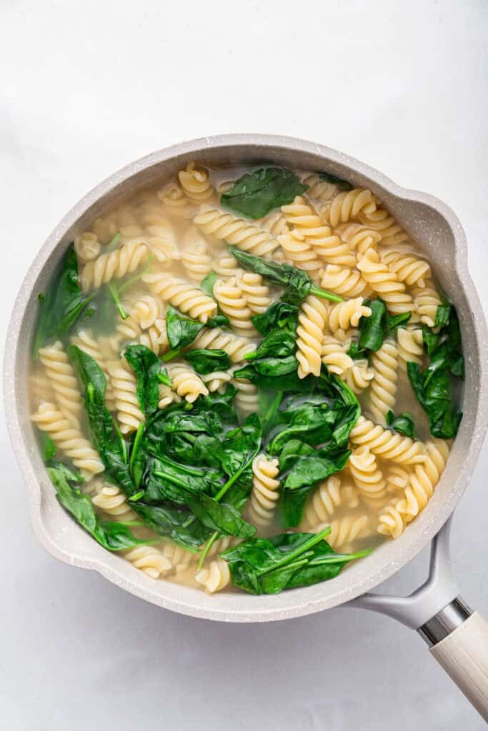 Overhead view of spinach and pasta in pot of water