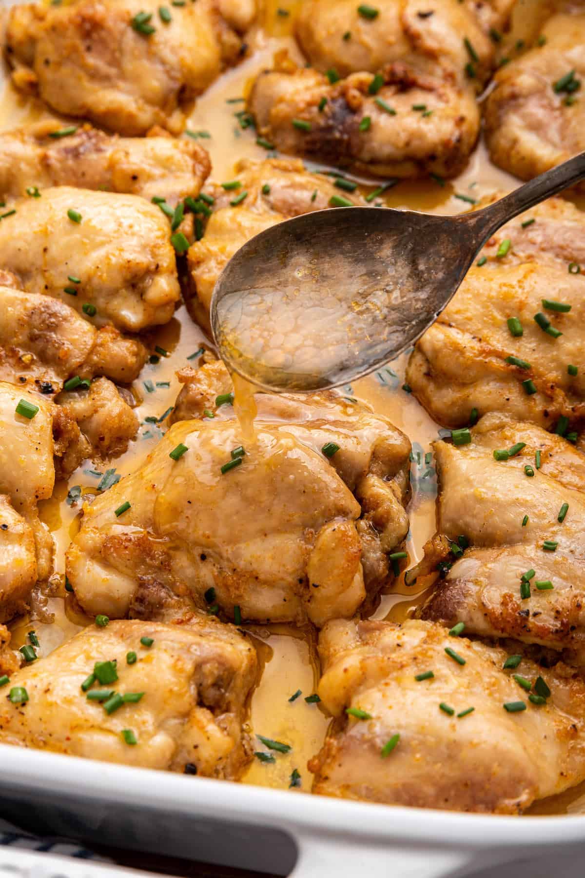 Spooning juices over baked boneless chicken thighs in baking dish