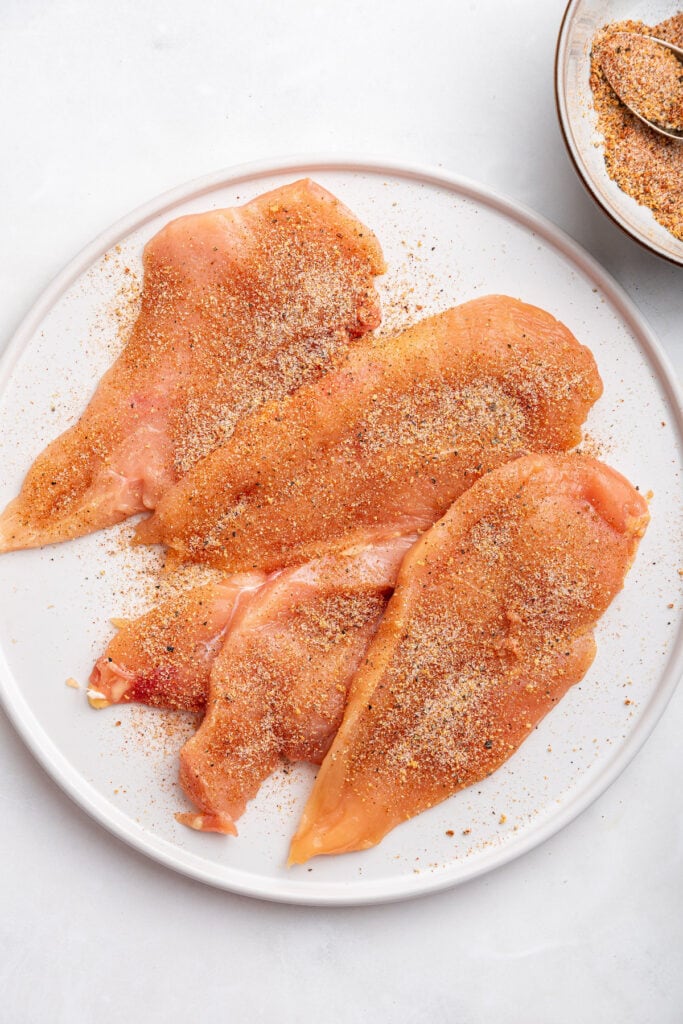 Pounded out chicken breast on plate with seasoning