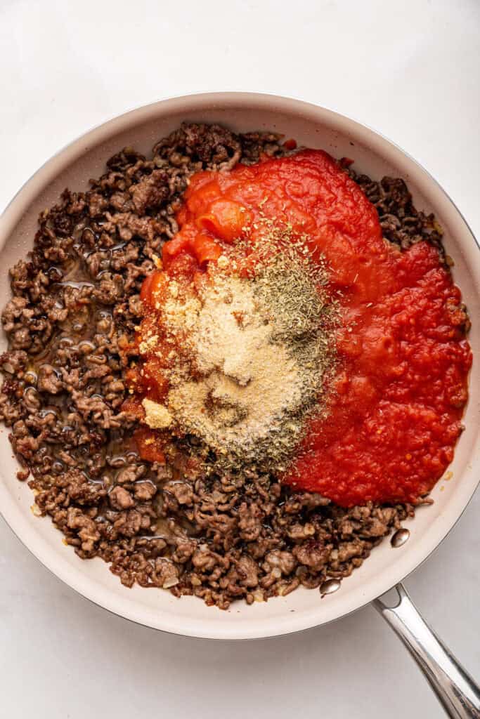 Adding seasonings and tomato sauce to ground beef in skillet