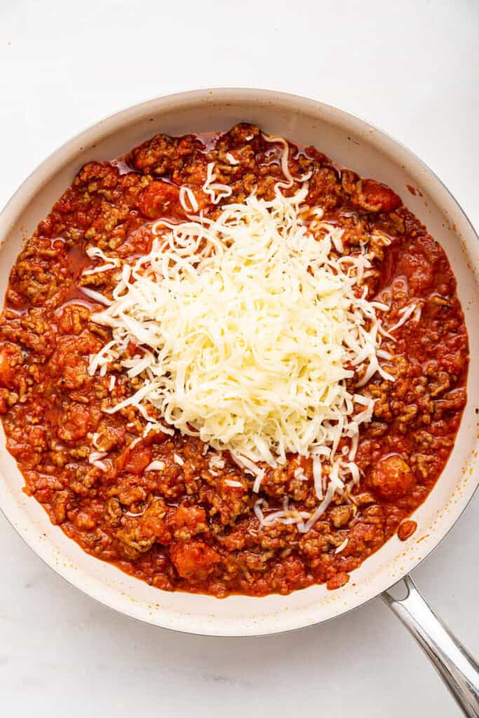 Adding cheese to skillet of meat sauce