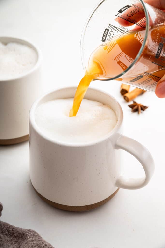 Pouring chai concentrate into mug of frothed milk