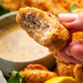 Hand holding chicken nugget, bitten to show inside