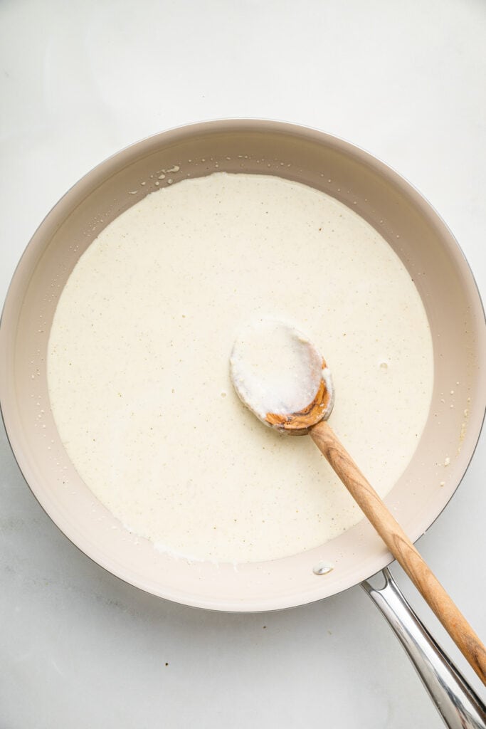 Overhead view of creamy cottage cheese Alfredo sauce in skillet with wooden spoon