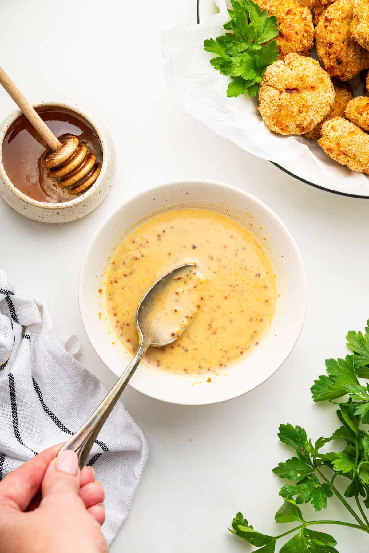 Spoon stirring honey mustard dipping sauce in bowl