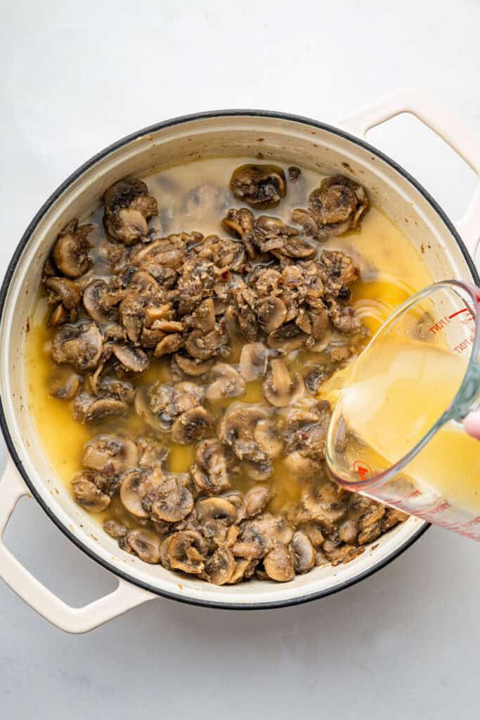 Pouring broth into pan of mushrooms