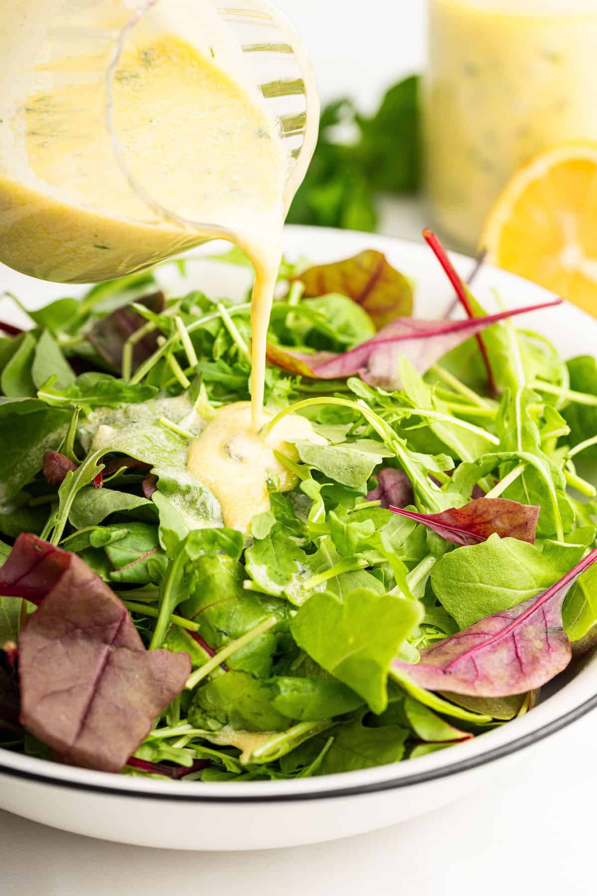 Pouring Italian dressing onto bowl of greens