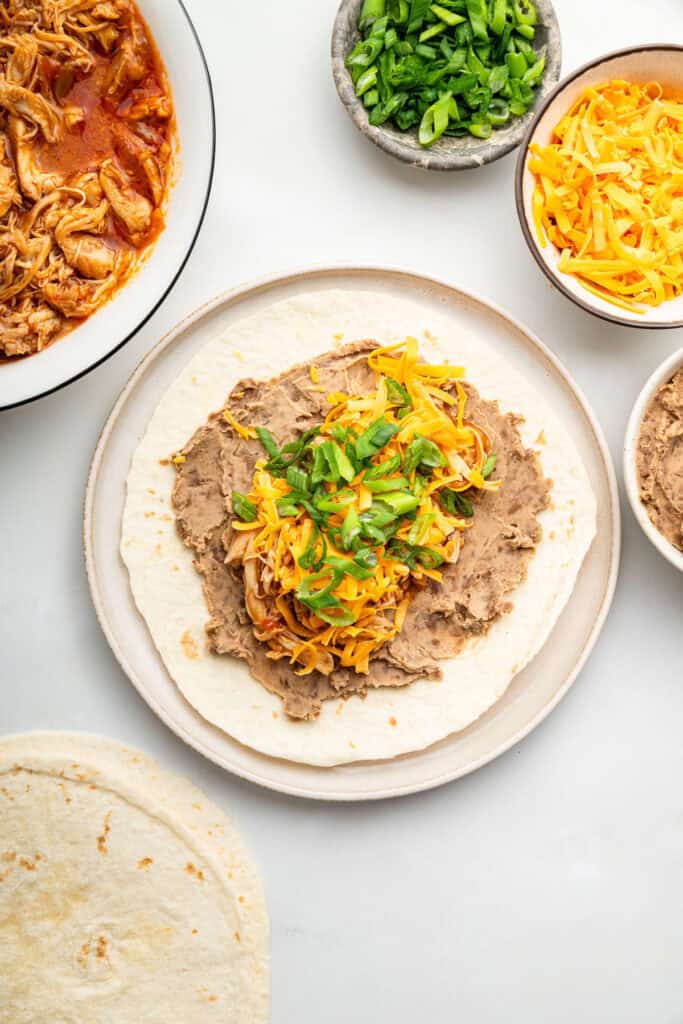 Filling chimichanga with cheese, green onions, chicken, and beans