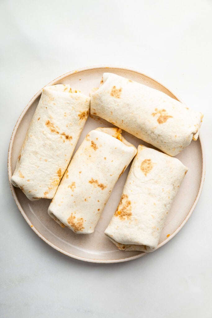 Wrapped chimichangas on plate before cooking