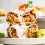 Two halves of an air fryer chimichanga stacked on plate with crema