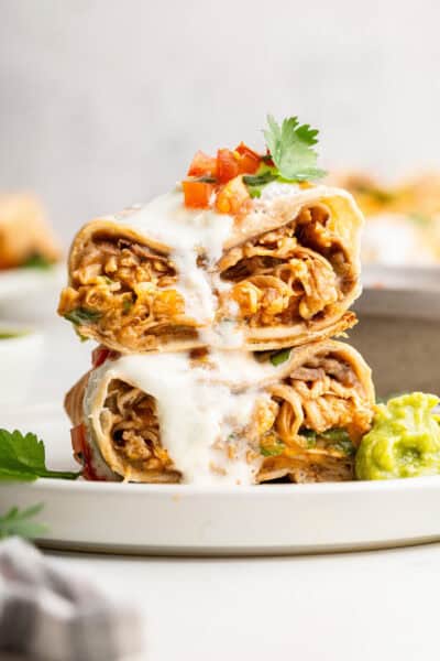 Two halves of an air fryer chimichanga stacked on plate with crema