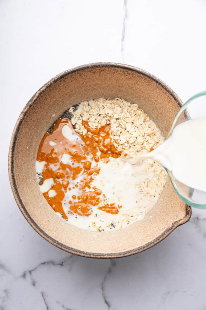 Pouring almond milk into bowl for overnight oats