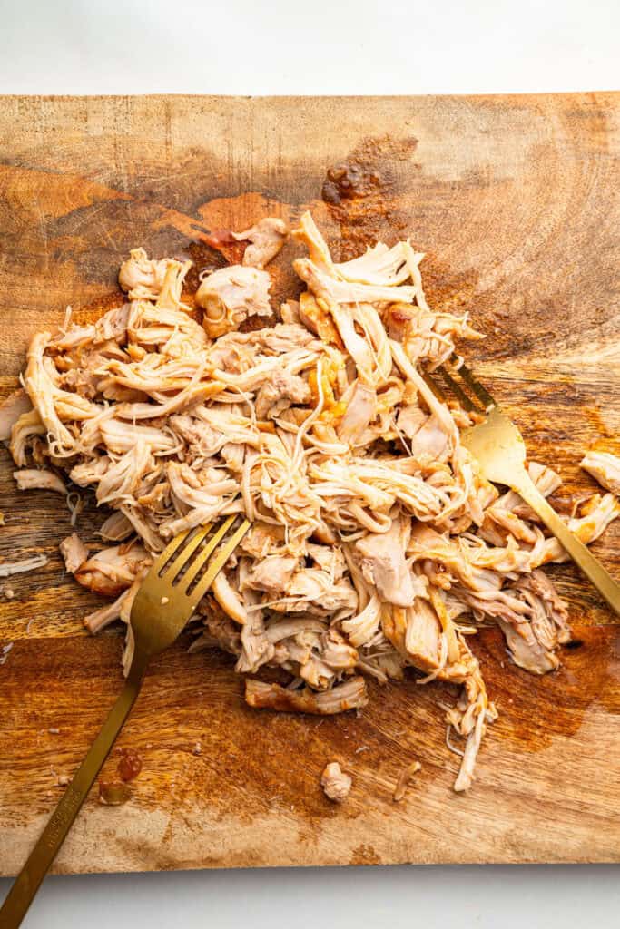 Overhead view of chicken being shredded on wooden board