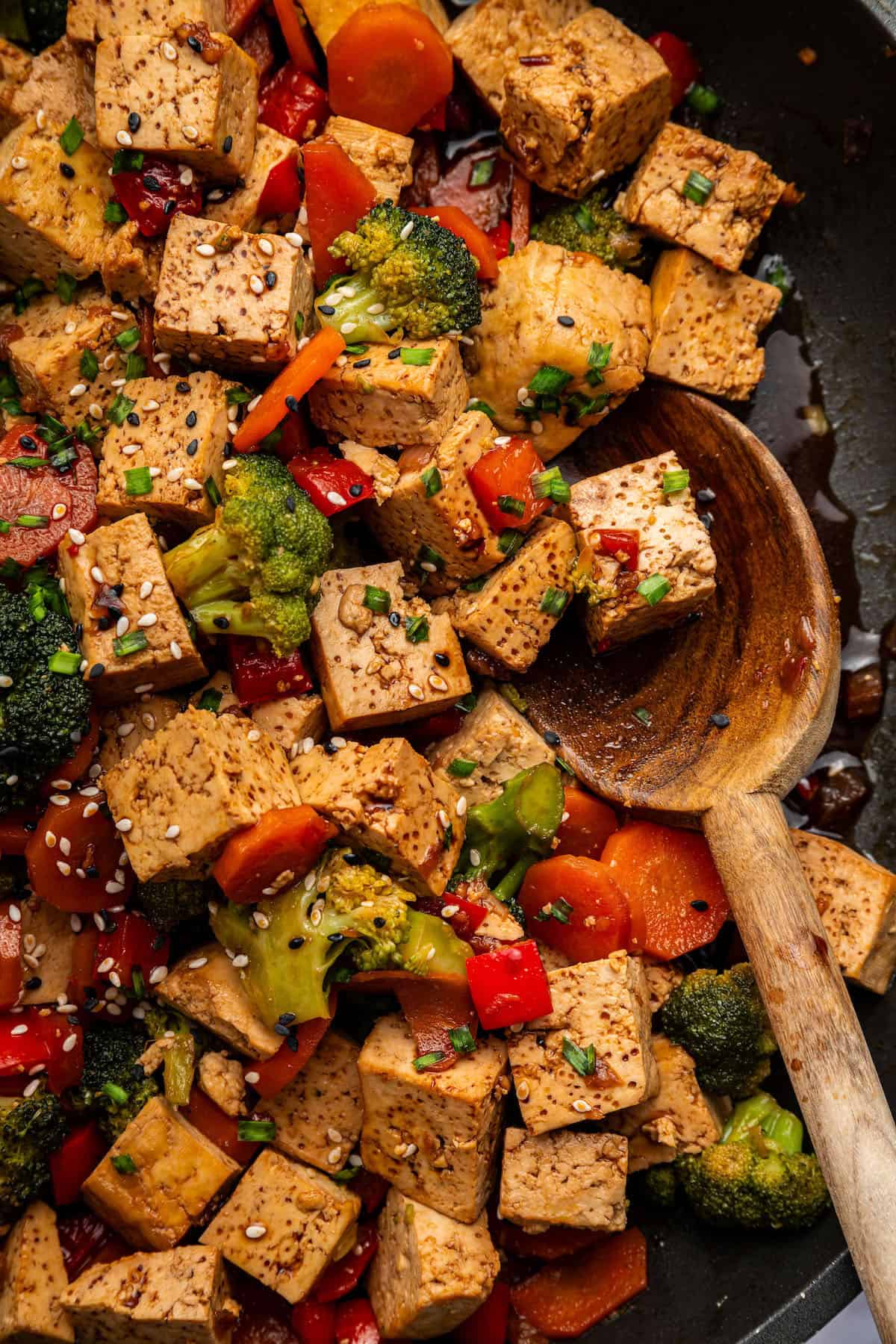 Spoon scooping tofu stir fry from pan