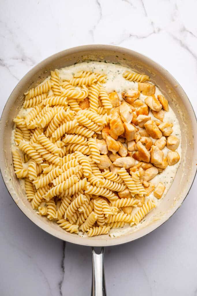 Overhead view of pasta and chicken added to sauce in skillet